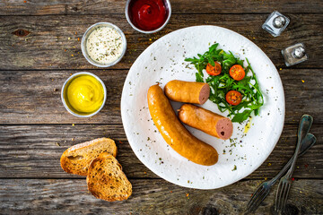 Breakfast - boiled sausages, bread and fresh vegetables served on wooden table
