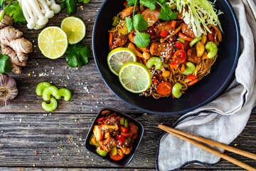Asian food - chicken nuggets, noodles, stir fried vegetables, soy sauce, cabbage and shimeji mushrooms on wooden table
