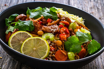 Asian food - chicken nuggets, noodles, stir fried vegetables, soy sauce, cabbage and shimeji mushrooms on wooden table
