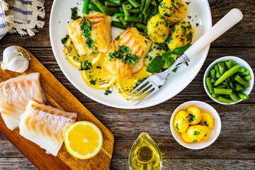 Fish dish - fried halibut with baked potatoes and boiled green beans on wooden table
