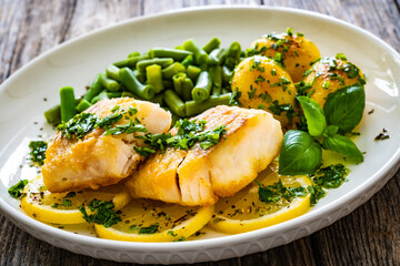 Fish dish - fried halibut with baked potatoes and boiled green beans on wooden table
