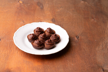 Chocolate candies on a white plate and on a wooden table