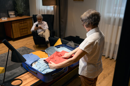 Old female helping husband fold clothes in trolley bag
