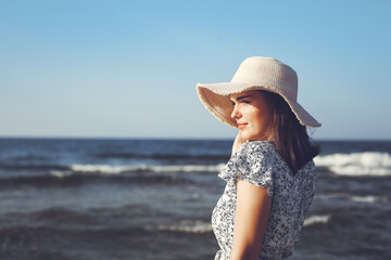 Happy brunette beautiful woman on the ocean beach standing in a white summer dress and glasses,...
