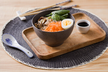 Shiitake mushrooms and soba noodle soup with carrot, spinach, boiled quail egg, and soy sauce on a wooden tray - 575292468