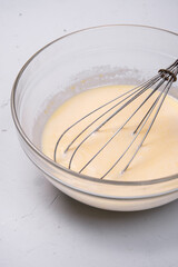 A mixture of milk and eggs is stirred with a whisk in a glass bowl