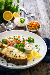 Fish dish - fried halibut with white rice, peas and carrots on wooden table
