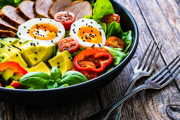 Tasty salad - roasted veal loin, avocado, boiled eggs and fresh vegetables on wooden table
