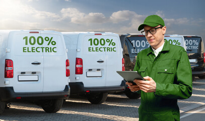 A man with a digital tablet stands next to electric delivery vans 