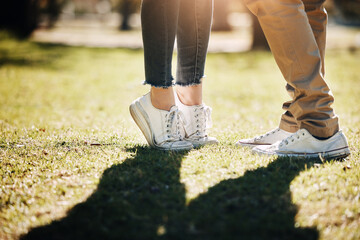Shoes, grass and love with a couple outdoor together, kissing for romance, dating or affection in...