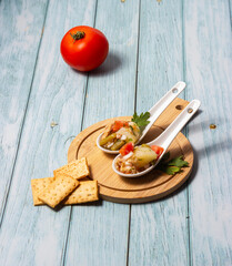 Appetizers of potato salad, tomato, green beans, egg and tuna in ceramic spoons on a wooden board