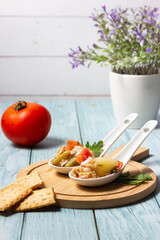 Appetizers of potato salad, tomato, green beans, egg and tuna in ceramic spoons on a wooden board