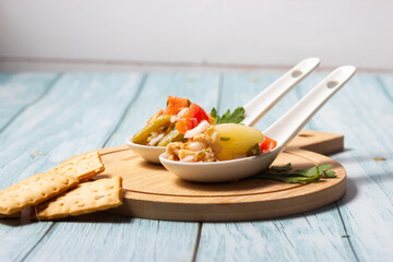 Close-up of appetizers of potato salad, tomato, green beans, egg and tuna in ceramic spoons on a wooden board