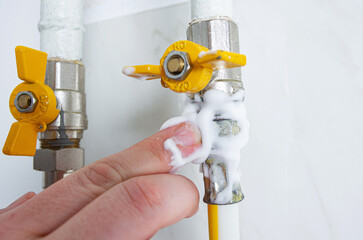A man applies soap foam to the connection of a gas valve and a flexible hose. A simple and cheap...