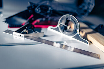 A piece of wood is set to be cut on a table saw, with a combination ruler that includes an angle ruler and a high-precision protractor placed on its surface for measuring purposes.