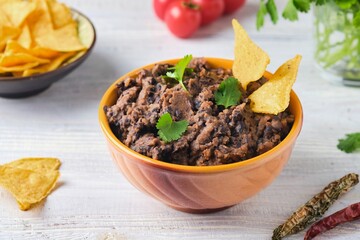 Refried beans, a dish of black beans, fried onions and spices in a yellow ceramic bowl on a light wooden background. Bean dishes. Vegan, lenten food.