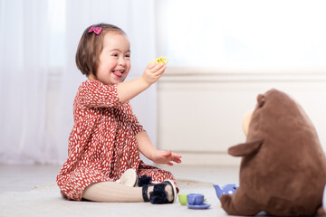 inclusion of children with down syndrome, cute friendly girl in kindergarten playing toys on the floor