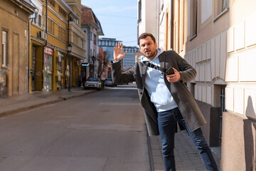 Man in coat standing on curbside hailing a taxi waving his hand.