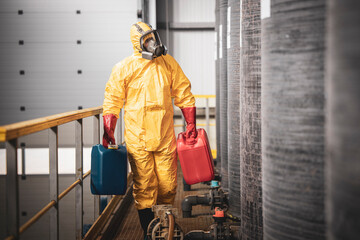 Fototapeta premium Industrial worker in protection suit and gas mask carrying plastic canisters with chemicals.