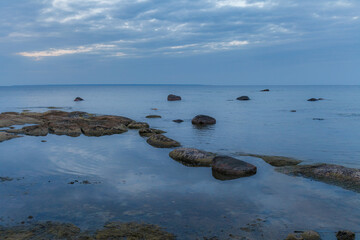 Fototapeta premium Beautiful sea shore view with with moss-covered rocks. Algae growing on seaside rocks. Blue hour time