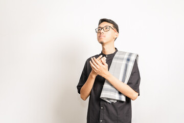A male single model doing pray with his two hands held together and looking up. Indonesian or southeast asian. Studio photoshoot with white background.