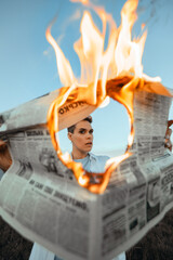 Portrait of a girl holding a burning newspaper with news.