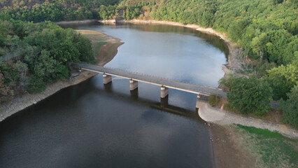 Aerial view of a bridge crossing a lake in summer, surrounded by the green forest and fields.