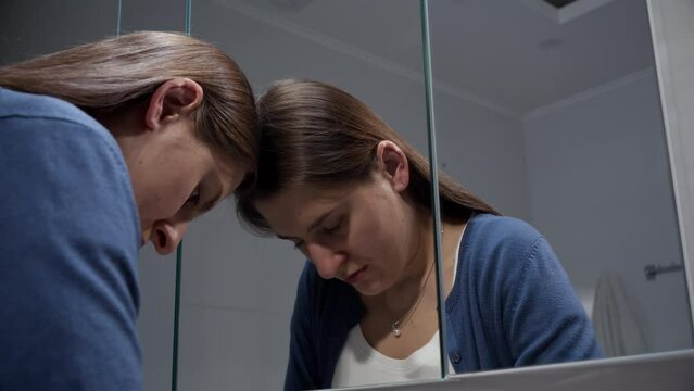 Portrait of angry and stressed woman leaning on mirror and looking in reflection. Concept of depression, suicide, stress, mental illness, loneliness and frustration