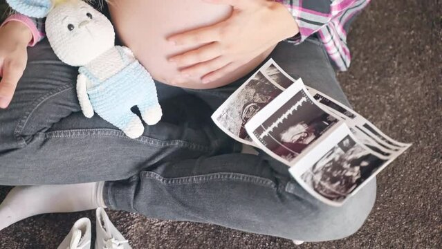 Ultrasound scan pictures to reveal baby gender, happy mother sitting on the floor and stroking gently her pregnant belly, medical examination before childbirth, maternity concept