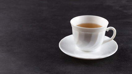 There is a white mug with tea on the table. On a black background.