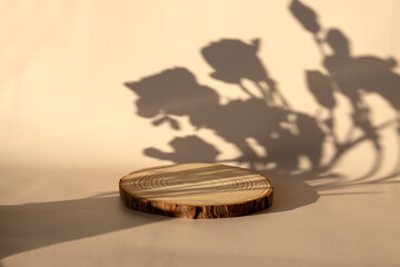Wooden slice of wood on a beige background with a shadow of flowers. Layout for a cosmetic product.