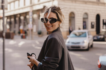 Obraz premium Young beautiful smiling hipster woman in trendy outfit. Sexy carefree woman posing on the street. Cheerful and happy in black sunglasses and grey suit turn around. Lifestyle, female beauty concept.