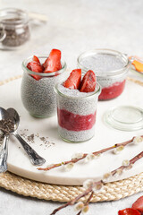 Breakfast idea - glass mason jars with chia seeds pudding, frozen strawberries and red raspberry smoothie on round marble board with easter decoration: spring branch of willow