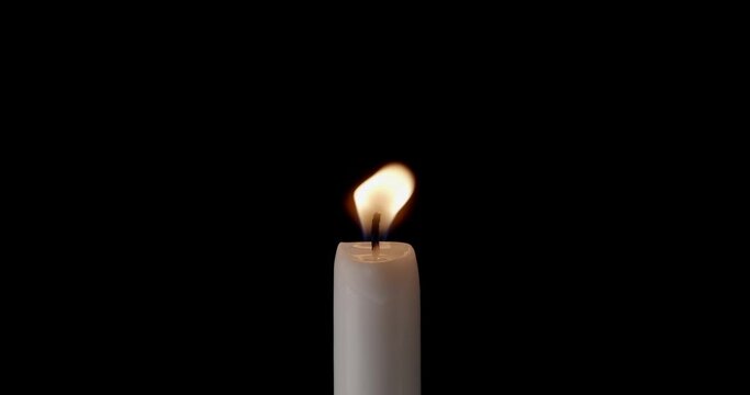 A single white candle burning. Isolated candle burning with dark background. White paraffin candle with yellow shades burns on a black background. Background of remembrance or celebration.