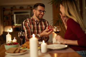 Delighted woman looking at her boyfriend while getting a marriage proposal over romantic dinner at home