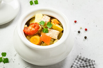 Stewed pork with root vegetables in ceramic pot. Top view, copy space.