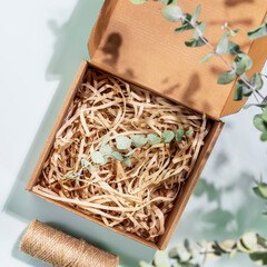 Eco friendly packaging concept. Cardboard box with shredded paper and eucalyptus sprig on blue background with green leaves and shadows. Eco packaging goods from online stores and delivery. Flat lay