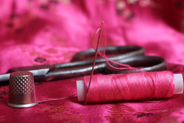 Spool of Pink Thread and Thimble on Vintage Pink Satin Fabric