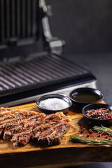 ribeye steak on wooden board with spices and electric grill