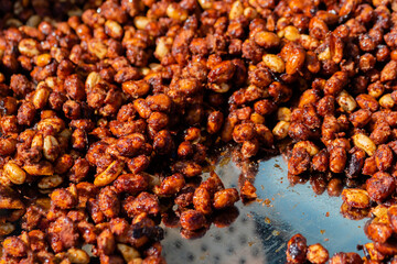 Heap of roasted caramelized sugared peanuts with warm and contrast sunlight illumination at summer outdoor food market - close up. Cookery, dessert, gastronomy and street food concept