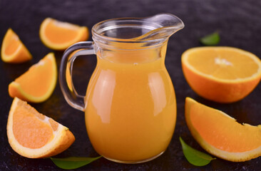 Organic orange juice in a glass decanter on a black background.
