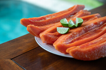 Sliced papaya with lime on table near swimming pool