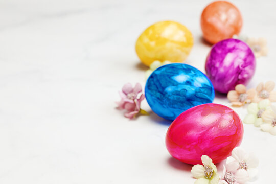 Easter eggs painted in pastel colors on a white background with copy space and cute spring flowers, Happy Easter Holiday concept with space for text. Yellow pink and blue