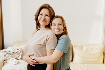 Teenage daughter affectionately hugging her mother smiling and looking at the camera
