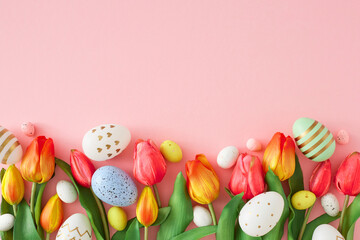Easter concept. Top view photo of red tulips flowers colorful eggs on isolated pastel pink background with empty space. Holiday card idea