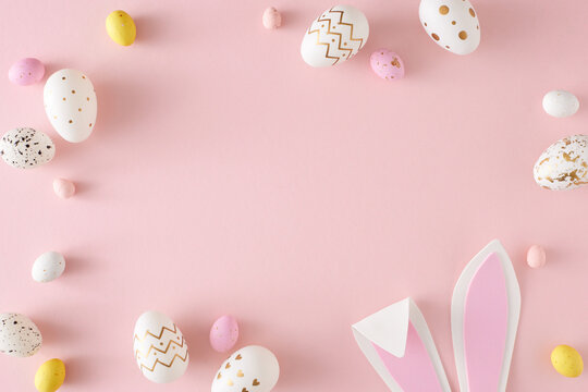 Easter party concept. Flat lay photo of yellow pink white eggs easter bunny ears on isolated pastel pink background with empty space. Holiday card idea