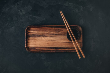 Empty wooden sushi plate with chopsticks on dark black stone background