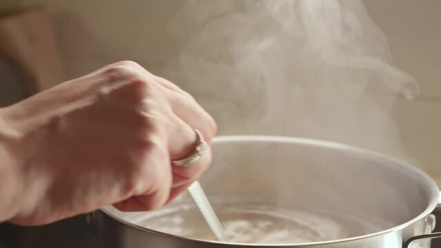 Closeup of woman stirring ingredients in pot while cooking soup. Healthy nutrition, cooking at home, hot steam