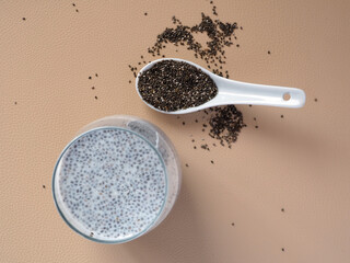 Milk pudding with chia seeds on a beige table and ceramic spoon with dry chia seeds.