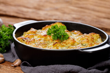 Potato casserole with cheese and parsley on wooden table. French cuisine, close up. Free space for text
